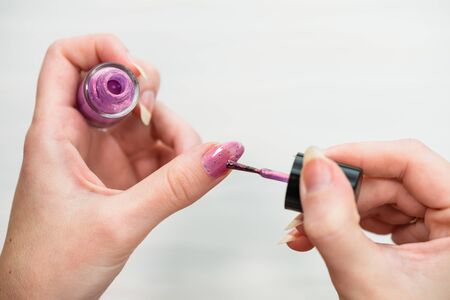 Female hands doing manicure, nail polish in gold glitter color on a white background. Skin and nail care salon conceptの写真素材