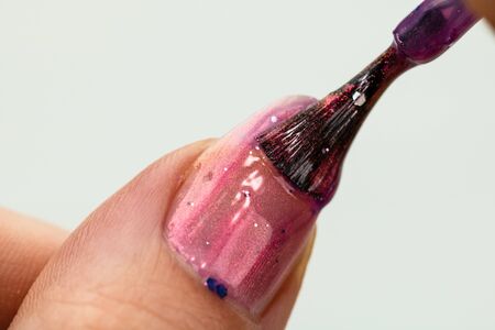 Female hands doing manicure, nail polish in gold glitter color on a white background. Skin and nail care salon conceptの写真素材