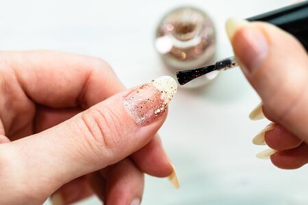 Female hands doing manicure, nail polish in gold glitter color on a white background. Skin and nail care salon conceptの写真素材
