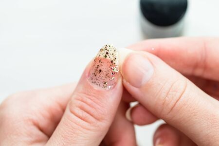 Female hands doing manicure, nail polish in gold glitter color on a white background. Skin and nail care salon conceptの写真素材