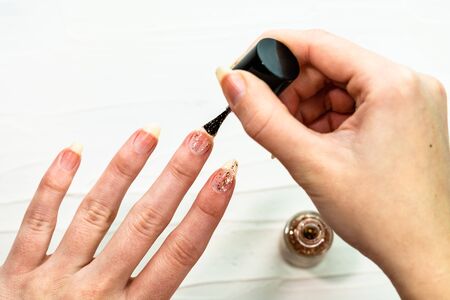 Female hands doing manicure, nail polish in gold glitter color on a white background. Skin and nail care salon conceptの写真素材