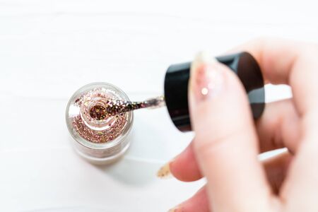 Female hands doing manicure, nail polish in gold glitter color on a white background. Skin and nail care salon conceptの写真素材