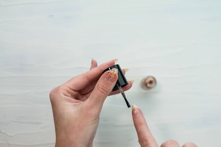 Female hands doing manicure, nail polish in gold glitter color on a white background. Skin and nail care salon conceptの写真素材