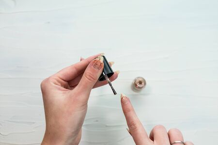 Female hands doing manicure, nail polish in gold glitter color on a white background. Skin and nail care salon conceptの写真素材