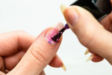 Female hands doing manicure, nail polish in gold glitter color on a white background. Skin and nail care salon conceptの写真素材