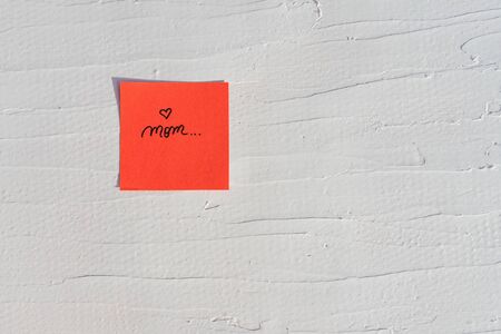 Handwriting text on memo post reminder. Mom and heart on paper, on white and textured wall.  Copy space.の写真素材