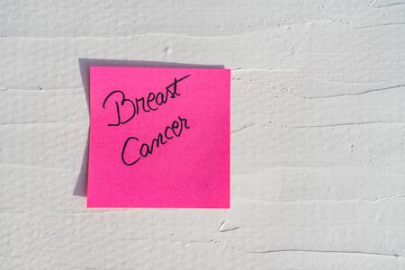 Handwriting text on memo post reminder. Breast Cancer on paper, on white and textured wall.  Copy space.の写真素材