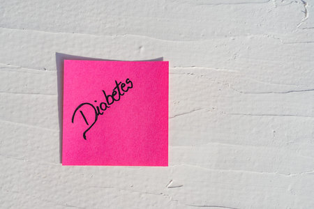 Handwriting text on memo post reminder. Diabetes on paper, on white and textured wall.  Copy space.