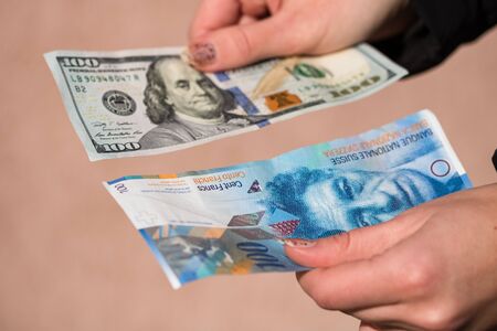 Hand holding money isolated on banknotes background. USD and CHF currency banknotes compared close up. Inflation, finance and business conceptのeditorial素材