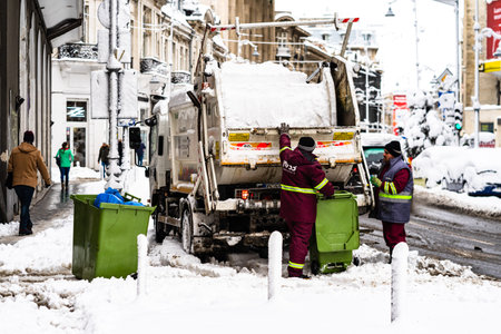 Employees loading a garbage truck in the morning. Winter season and icy cars on the road in morning...