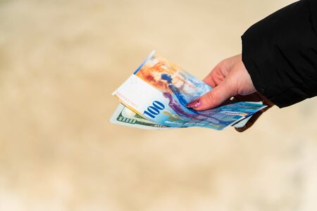 Woman hand holding and giving money. World money concept, close up of 100 swiss franc banknote and 100 US dollar, photo of CHF and USD currencyの写真素材