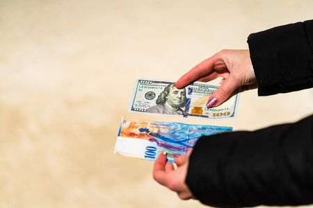 Woman hand holding and giving money. World money concept, close up of 100 swiss franc banknote and 100 US dollar, photo of CHF and USD currencyの写真素材