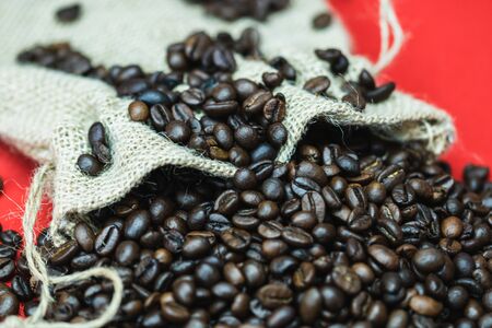 Roasted coffee beans in a burlap sack, sackcloth bag with coffee beans on red background, top view, coffee conceptの写真素材
