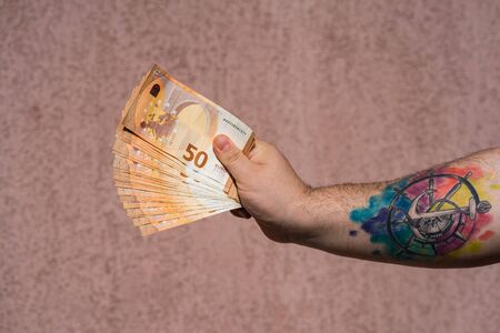 Hand with tattoo holding and showing a fan of euro money or giving money. World money concept, 50 EURO banknotes EUR currency isolated. Bucharest, Romania, 2020.のeditorial素材