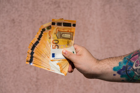 Hand with tattoo holding and showing a fan of euro money or giving money. World money concept, 50 EURO banknotes EUR currency isolated. Bucharest, Romania, 2020.のeditorial素材
