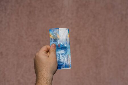 Hand holding showing euro money and giving or receiving money like tips, salary. 100 swiss franc banknotes CHF currency isolated. Concept of rich business people, saving or spending money.の写真素材