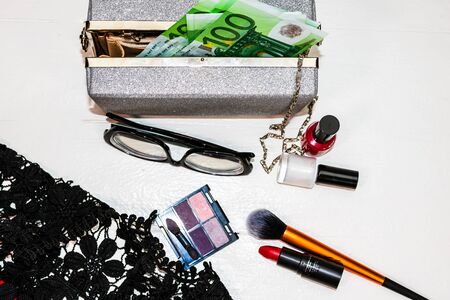 Glittery silver clutch bag with money and beauty products isolated on white background with copy space.の写真素材