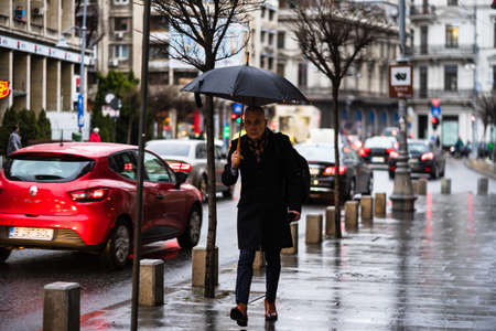 Old man with umbrella walking on a rainy day on the main boulevard of Bucharest city, Romania 2020のeditorial素材