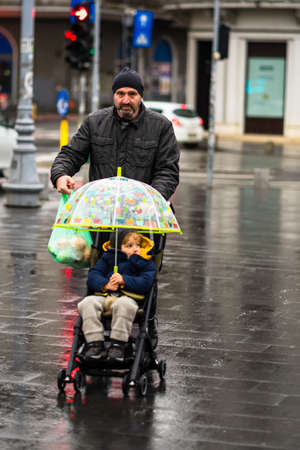 Man with kid on a baby stroller walking on a rainy day on the main boulevard of Bucharest city, Romania 2020のeditorial素材