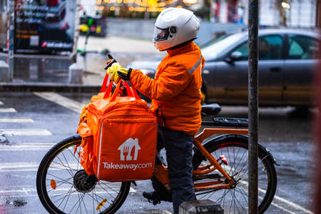Young man on an electric bike with takeaway.com logo delivering food during a rainy day in Bucharest, Romania, 2020のeditorial素材