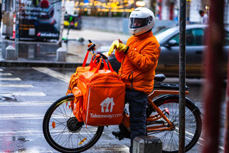 Young man on an electric bike with takeaway.com logo delivering food during a rainy day in Bucharest, Romania, 2020のeditorial素材