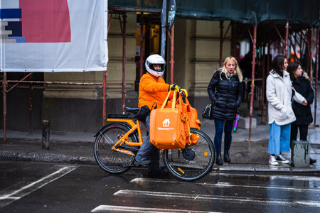 Young man on an electric bike with takeaway.com logo delivering food during a rainy day in...