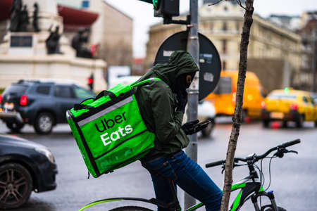 Young man on a bike with Uber Eats logo delivering food during a rainy day in Bucharest, Romania, 2020のeditorial素材