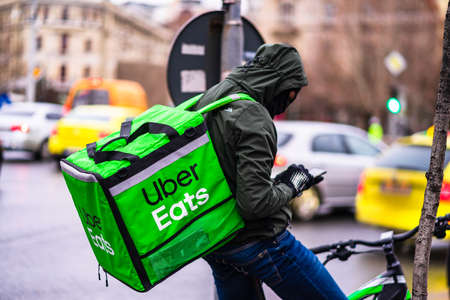 Young man on a bike with Uber Eats logo delivering food during a rainy day in Bucharest, Romania, 2020のeditorial素材