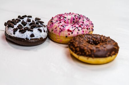 Colorful donuts on white wooden table. Sweet icing sugar food with glazed sprinkles, doughnut with frosting. Top view with copy spaceの写真素材