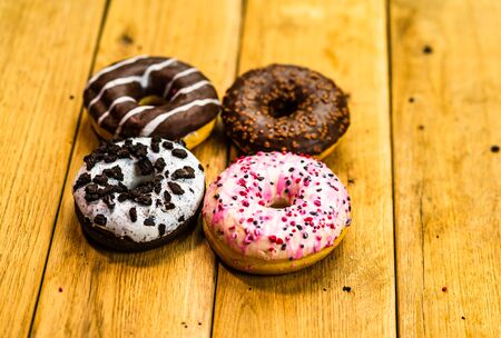 Colorful donuts on wooden table. Sweet icing sugar food with glazed sprinkles, doughnut with chocolate frosting. Top view with copy spaceの写真素材
