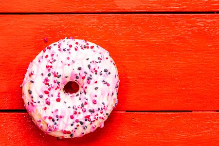 Colorful donuts on red wooden table. Sweet icing sugar food with glazed sprinkles, doughnut with chocolate frosting. Top view with copy spaceの写真素材