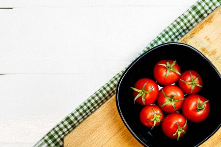 Top view of fresh ripe cherry tomatoes in small black bowl on a rustic white wooden table. Ingredients and food conceptの写真素材