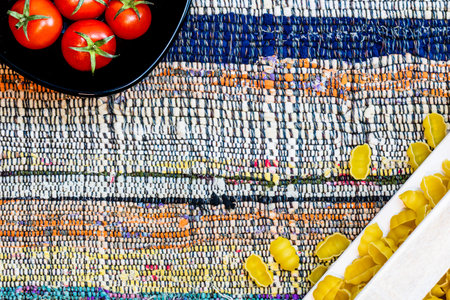 Top detail view of pasta in a wooden crate and fresh ripe cherry tomatoes in a black bowl on a rustic napkin. Ingredients and food conceptの写真素材