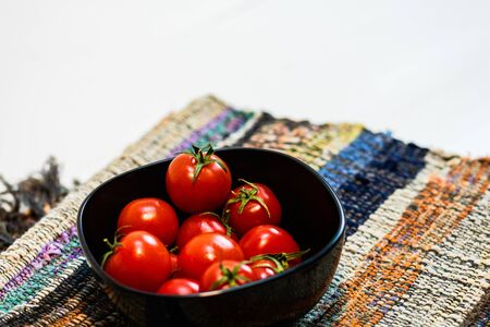 Detail of ripe cherry tomatoes in small black bowl on a rustic napkin. Ingredients and food conceptの写真素材
