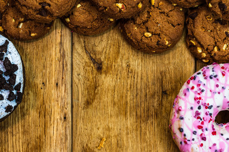 Frame made of chocolate chip cookies, biscuits and colorful donuts top view with copy space.