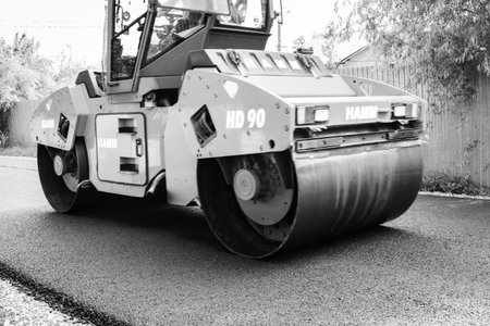 Workers and asphalting machines. Heavy road roller in motion on the roadway. Construction of a new...