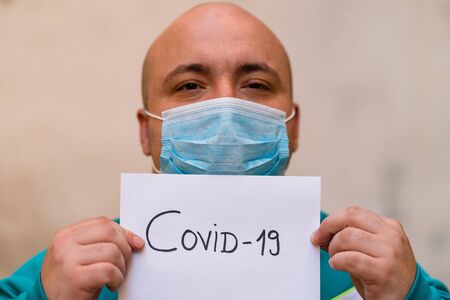 Sick young man with medical face mask close up portrait. Man holding message on a paper on blurred background. Covid-19 outbreak contamination conceptの写真素材