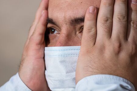 Sick young man with headache and medical protective face mask illustrates pandemic coronavirus disease on blurred background. Covid-19 outbreak in Europeの写真素材