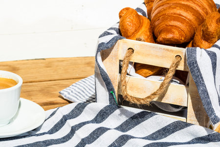 Puff pastry, coffee cup and buttered French croissant on wooden crate. Food and breakfast concept....