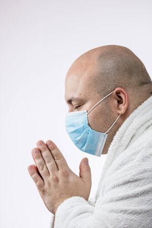 Caucasian sick young man with medical protective face mask praying to God, isolated on white. Covid 19 disease, Covid-19 outbreak, flu contamination and healthcare conceptの写真素材