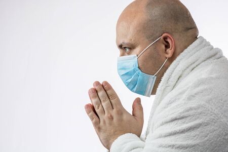 Caucasian sick young man with medical protective face mask praying to God, isolated on white. Covid 19 disease, Covid-19 outbreak, flu contamination and healthcare conceptの写真素材
