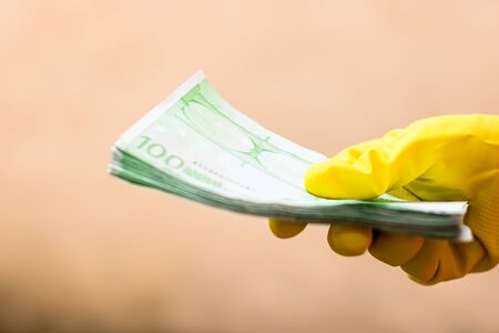 World money concept, hand with gloves receiving, giving or holding 100 EURO banknote, isolated on blurred background. Corona virus COVID-19 outbreak. Concept of prevention virus spreadの写真素材