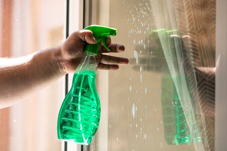 Man cleaning window using window cleaning squeegee and cleaning sprayer, cleaning services concept. Housework and housekeeping conceptの写真素材