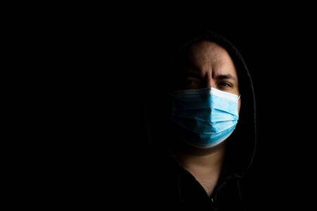 Caucasian young man with medical protective face mask illustrates pandemic coronavirus, Covid 19 disease isolated on black copy space. Covid-19 outbreak, flu contamination and healthcare conceptの写真素材
