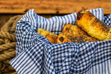 Sausages baked in dough sprinkled with salt and poppy seeds in a rustic composition. Sausages rolls, delicious homemade pastries.の写真素材