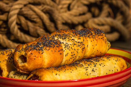 Sausages baked in dough sprinkled with salt and poppy seeds in a rustic composition. Sausages rolls, delicious homemade pastries.の写真素材