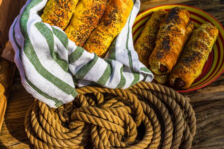 Sausages baked in dough sprinkled with salt and poppy seeds in a rustic composition. Sausages rolls, delicious homemade pastries.の写真素材