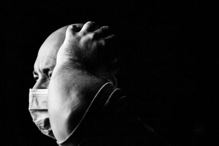 Pandemic home isolation, man with medical protective face mask isolated on black with copy spaceの写真素材