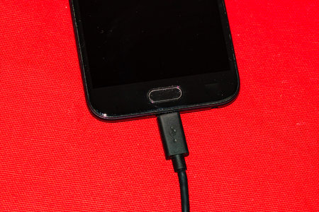 Close-up of black smartphone charging battery with an USB cable on wooden table with copy space .