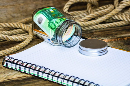 Composition with saving money banknotes in a glass jar with spiral notebook. Concept of investing...